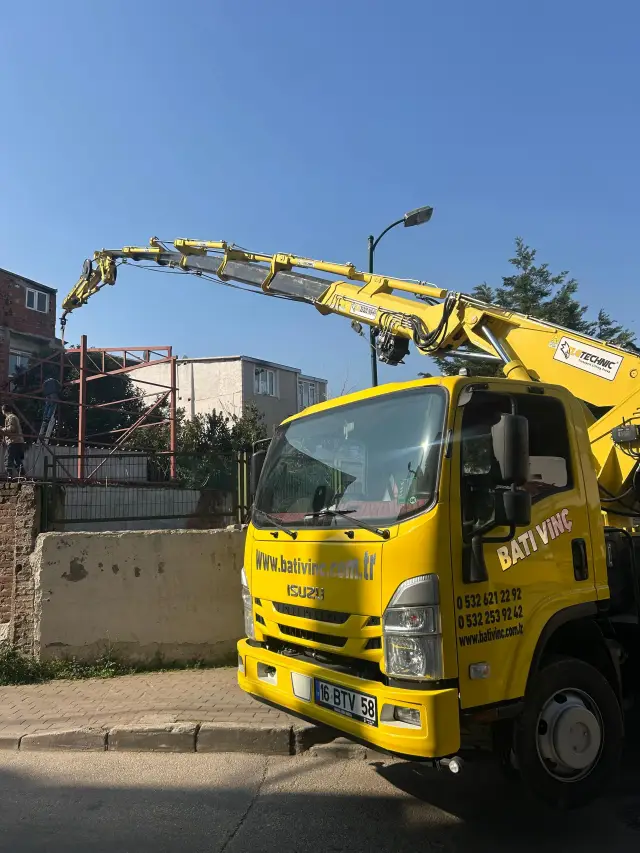 Şehir içinde bir binanın çatısına malzeme kaldıran kamyon üstü vinç
